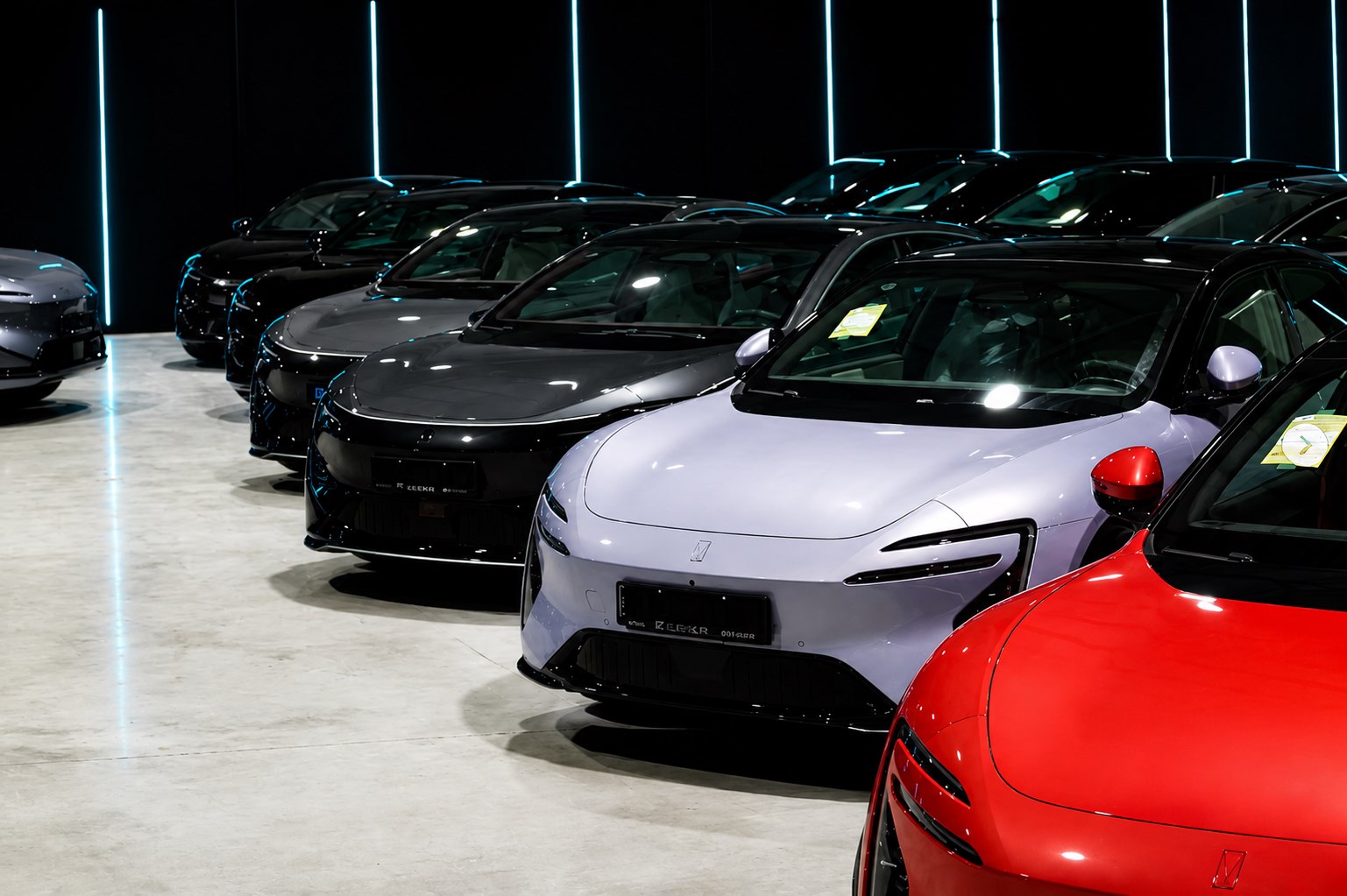 A row of electric vehicles in the FluxFusion Kosova showroom, lit by blue accent strips