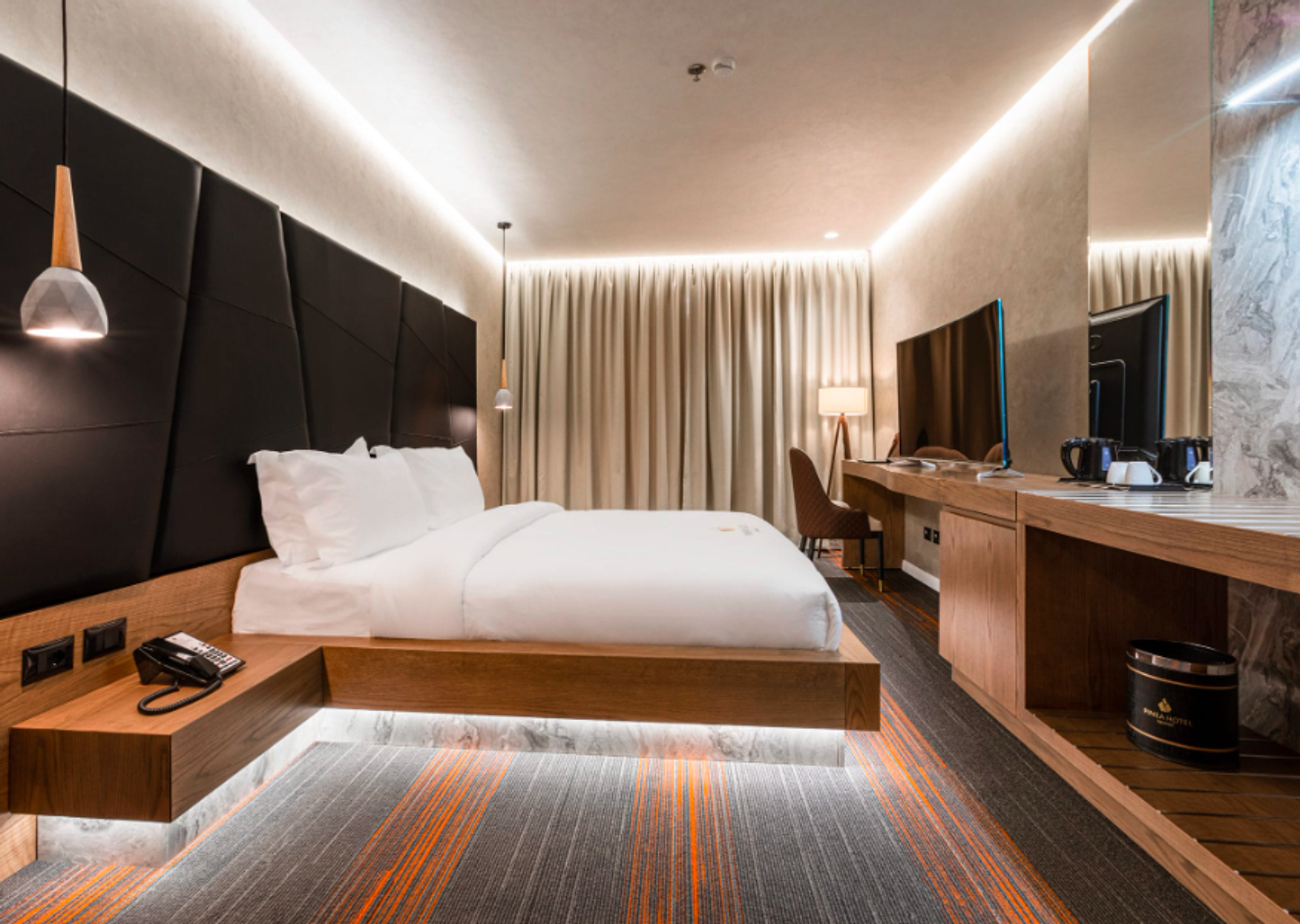 A Hotel Pinea Standard room, dark upholstered headboard and a desk beside the window